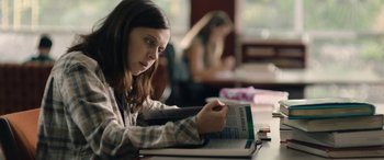 Movie still from “Wildling” (2018), directed by Fritz Böhm – A woman sitting at a table with a book in her hands; Medium shot, Over the shoulder angle