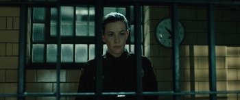 Movie still from “Wildling” (2018), directed by Fritz Böhm – A woman in a police uniform behind bars in front of a clock; Medium shot, Low angle