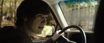 Movie still from “Wildling” (2018), directed by Fritz Böhm – A young man driving a car in the daytime; Close Up shot, Over the shoulder angle