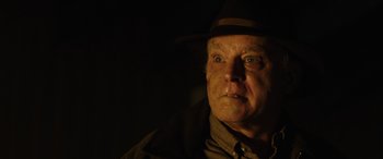 Movie still from “Wildling” (2018), directed by Fritz Böhm – An older man wearing a hat and a brown jacket; Close Up shot, Over the shoulder angle