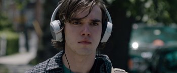 Movie still from “Wildling” (2018), directed by Fritz Böhm – A young man wearing white headphones while standing outside; Close Up shot, Over the shoulder angle