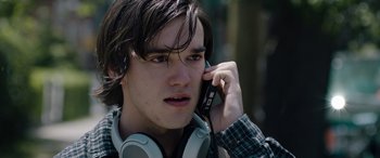 Movie still from “Wildling” (2018), directed by Fritz Böhm – A young man wearing headphones talking on a cell phone; Close Up shot, Over the shoulder angle