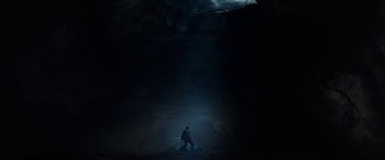 Movie still from “Wildling” (2018), directed by Fritz Böhm – A man standing in a dark cave with a light shining on him; Extreme Wide shot, Low angle