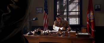 Movie still from “Windtalkers” (2002), directed by John Woo – A man sitting at a desk in front of an american flag; Medium shot, High angle