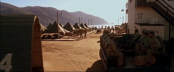 Movie still from “Windtalkers” (2002), directed by John Woo – A group of men sitting on a bench in front of tents on the beach; Extreme Wide shot, High angle