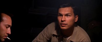 Movie still from “Windtalkers” (2002), directed by John Woo – A man sitting in a dark room looking at the camera; Close Up shot, High angle