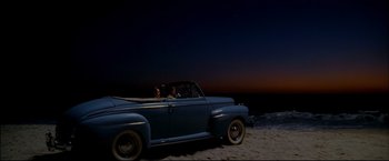 Movie still from “Windtalkers” (2002), directed by John Woo – A man driving an old car on the beach at night; Extreme Wide shot, High angle