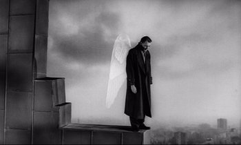 Movie still from “Wings of Desire” (1987), directed by Wim Wenders – A man standing on top of a building with a large angel wing; Wide shot, Low angle