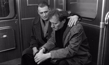 Movie still from “Wings of Desire” (1987), directed by Wim Wenders – A couple of men sitting next to each other on top of a bench; Medium shot, Low angle