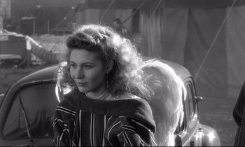 Movie still from “Wings of Desire” (1987), directed by Wim Wenders – A young woman with long curly hair standing in front of an antique car; Close Up shot, Over the shoulder angle