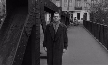 Movie still from “Wings of Desire” (1987), directed by Wim Wenders – A black and white photo of a man standing in a street; Wide shot, Low angle