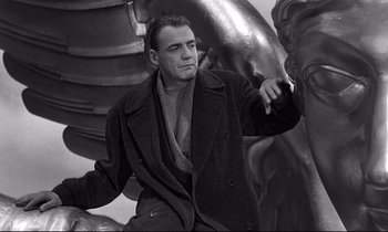 Movie still from “Wings of Desire” (1987), directed by Wim Wenders – A black and white photo of a man leaning against a statue; Medium shot, Low angle