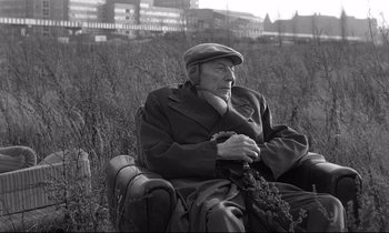 Movie still from “Wings of Desire” (1987), directed by Wim Wenders – An old man sitting in a chair in a field; Medium shot, Low angle