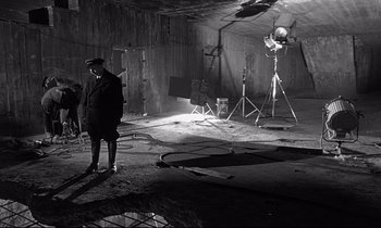 Movie still from “Wings of Desire” (1987), directed by Wim Wenders – A man standing in an empty room in front of a camera rig; Wide shot, High angle