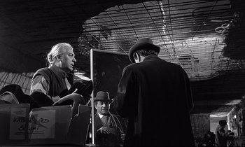 Movie still from “Wings of Desire” (1987), directed by Wim Wenders – A group of men standing next to each other in a room; Medium shot, Over the shoulder angle