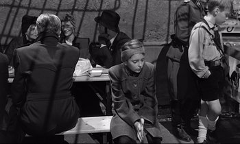 Movie still from “Wings of Desire” (1987), directed by Wim Wenders – A woman sitting on a bench in front of a group of people; Medium shot, High angle