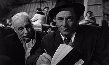 Movie still from “Wings of Desire” (1987), directed by Wim Wenders – An older man in a suit and tie next to an older woman in a hat; Close Up shot, Low angle