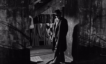 Movie still from “Wings of Desire” (1987), directed by Wim Wenders – A black and white photo of a man in a suit and hat; Wide shot, High angle