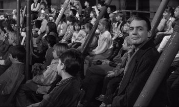 Movie still from “Wings of Desire” (1987), directed by Wim Wenders – A group of people sitting in a stadium watching a game; Medium shot, High angle