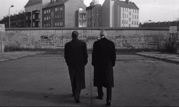 Movie still from “Wings of Desire” (1987), directed by Wim Wenders – A couple of men walking down a street; Wide shot, Low angle