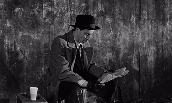 Movie still from “Wings of Desire” (1987), directed by Wim Wenders – A black and white photo of a man reading a newspaper; Medium shot, High angle