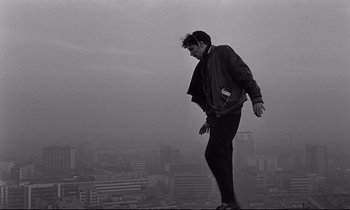 Movie still from “Wings of Desire” (1987), directed by Wim Wenders – A man standing on top of a tall building; Wide shot, Low angle