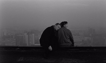 Movie still from “Wings of Desire” (1987), directed by Wim Wenders – Two men sitting on a ledge looking out at a city skyline; Medium shot, High angle
