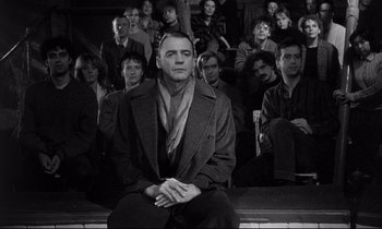 Movie still from “Wings of Desire” (1987), directed by Wim Wenders – Black and white photograph of a man sitting in front of a group of people; Medium shot, High angle
