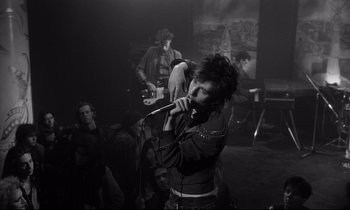 Movie still from “Wings of Desire” (1987), directed by Wim Wenders – A person with a microphone in front of a group of people; Medium shot, Low angle