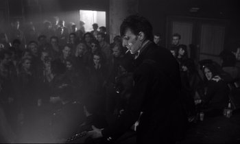 Movie still from “Wings of Desire” (1987), directed by Wim Wenders – A man smoking a cigarette in front of a crowd; Medium shot, Low angle