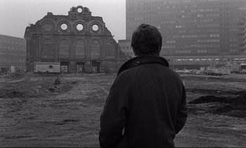Movie still from “Wings of Desire” (1987), directed by Wim Wenders – A man standing in front of an abandoned building; Wide shot, Over the shoulder angle