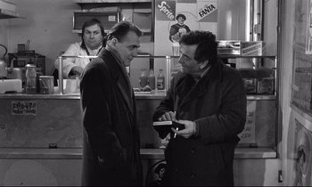 Movie still from “Wings of Desire” (1987), directed by Wim Wenders – A couple of men standing next to each other in a room; Medium shot, Over the shoulder angle
