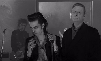 Movie still from “Wings of Desire” (1987), directed by Wim Wenders – A man in a suit and tie holding a microphone and another man in a suit and tie; Medium shot, Over the shoulder angle
