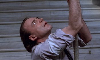 Movie still from “Wings of Desire” (1987), directed by Wim Wenders – A man holding onto a rope while looking up; Close Up shot, Low angle