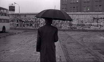 Movie still from “Wings of Desire” (1987), directed by Wim Wenders – A man holding an umbrella in front of a graffiti wall; Wide shot, Low angle