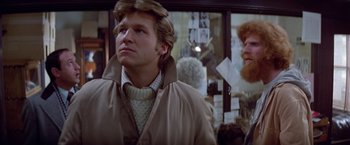 Movie still from “Winter Kills” (1979), directed by William Richert – A man wearing a tan jacket and a white sweater; Close Up shot, Over the shoulder angle
