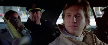 Movie still from “Winter Kills” (1979), directed by William Richert – A man sitting in the driver's seat of a car; Close Up shot, Low angle