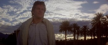 Movie still from “Winter Kills” (1979), directed by William Richert – A man standing next to a palm tree under a cloudy sky; Close Up shot, Low angle