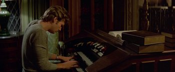 Movie still from “Winter Kills” (1979), directed by William Richert – A young man playing the piano in a room; Medium shot, High angle