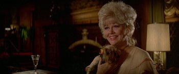 Movie still from “Winter Kills” (1979), directed by William Richert – An older woman holding a small dog in her arms; Close Up shot, Over the shoulder angle