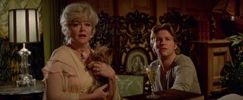 Movie still from “Winter Kills” (1979), directed by William Richert – A woman and a man sitting at a table with a dog; Close Up shot, Over the shoulder angle