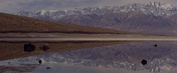 Movie still from “Winter Kills” (1979), directed by William Richert – A view of a mountain range and a body of water in front of it; Extreme Wide shot, High angle