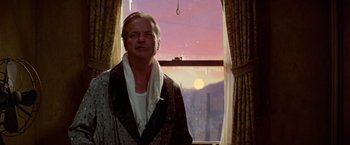 Movie still from “Winter Kills” (1979), directed by William Richert – A man standing in front of a window; Medium shot, Low angle