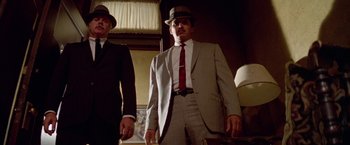 Movie still from “Winter Kills” (1979), directed by William Richert – A man in a suit and hat standing next to another man; Medium shot, Low angle