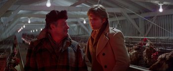 Movie still from “Winter Kills” (1979), directed by William Richert – Two men are standing in a warehouse talking to each other; Medium shot, Over the shoulder angle