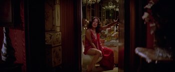 Movie still from “Winter Kills” (1979), directed by William Richert – A woman sitting on a toilet in a room; Wide shot, High angle