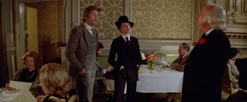 Movie still from “Winter Kills” (1979), directed by William Richert – A man and a woman standing next to each other in front of a table; Medium shot, Over the shoulder angle