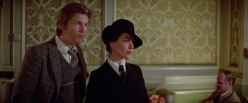 Movie still from “Winter Kills” (1979), directed by William Richert – A man and a woman wearing suits and a hat; Close Up shot, Low angle