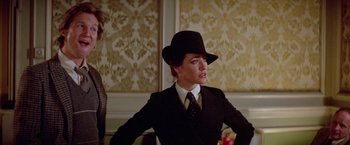 Movie still from “Winter Kills” (1979), directed by William Richert – A woman wearing a suit and a black hat; Medium shot, Over the shoulder angle