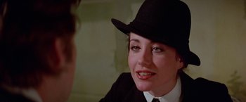 Movie still from “Winter Kills” (1979), directed by William Richert – A woman wearing a black hat and a white shirt; Close Up shot, Over the shoulder angle